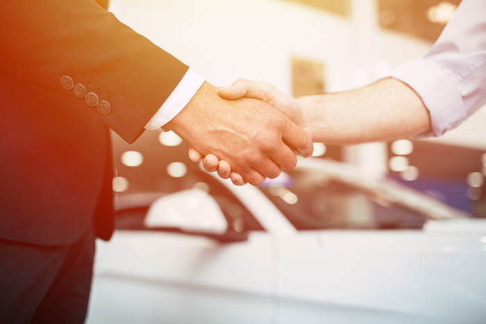 two people shaking hands in front of car